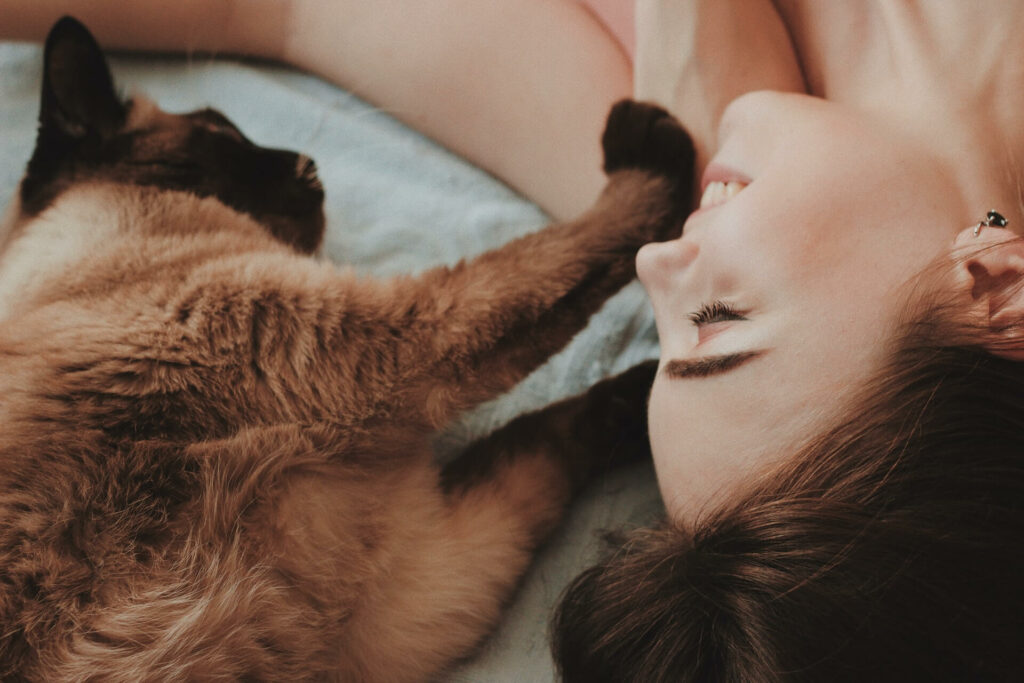 Kat en baasje liggen naast elkaar en kat raakt met pootjes zacht het gezicht van de vrouw aan
